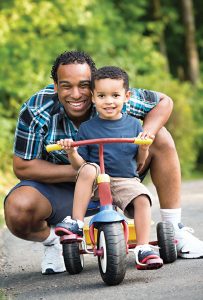 Little boy on a trike with his smiling dad