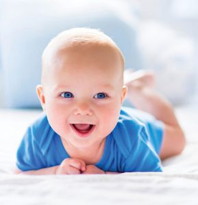 Smiling Infant in blue jumper laying on stomach.
